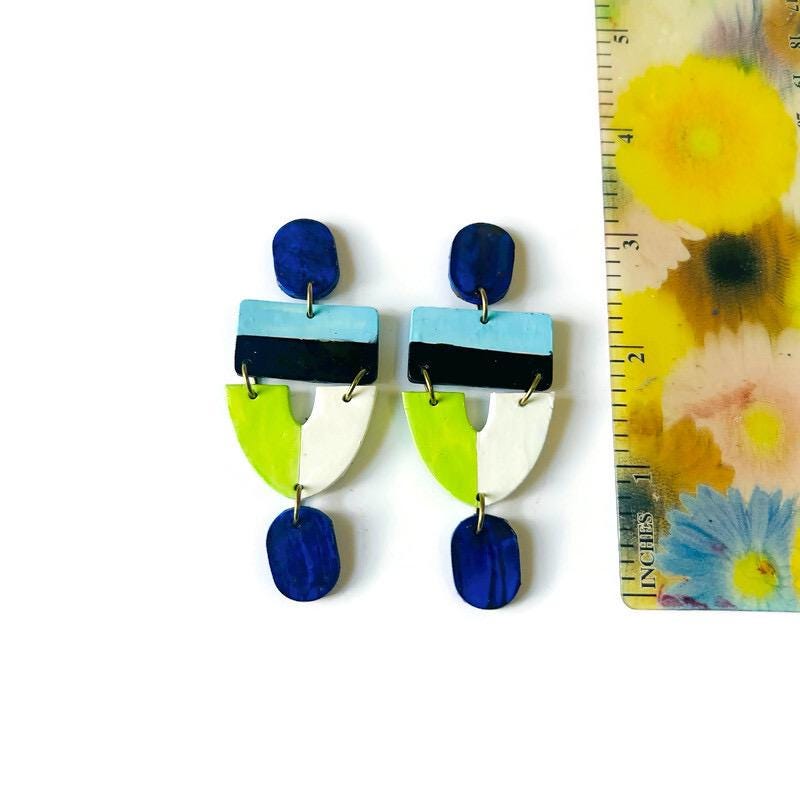 Colorful geometric earrings next to a floral-patterned ruler on a white background