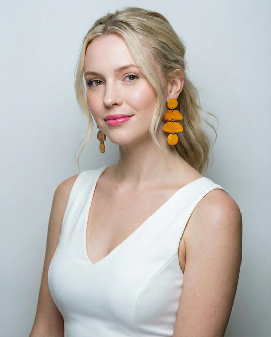Woman wearing a white dress and yellow earrings against a light gray background
