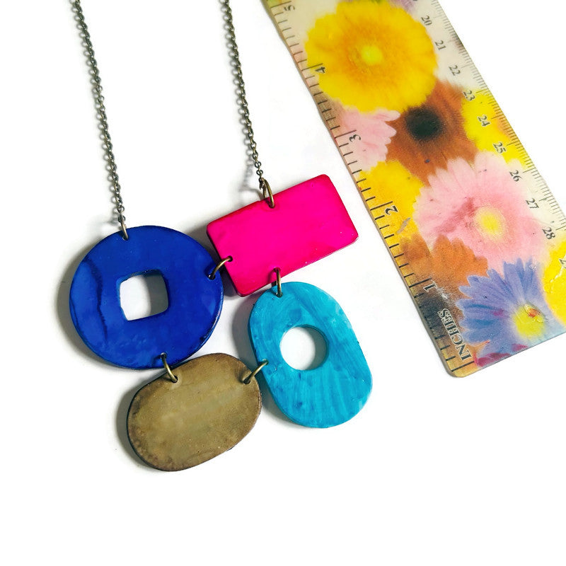 Necklace with colorful pendant next to a floral-patterned ruler on a white background