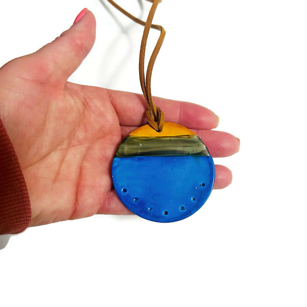 Hand holding a blue and yellow pendant with a white background