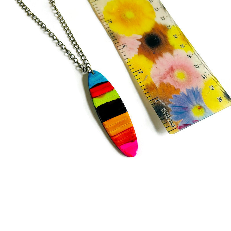 Colorful striped pendant on a chain with a ruler for scale against a floral background