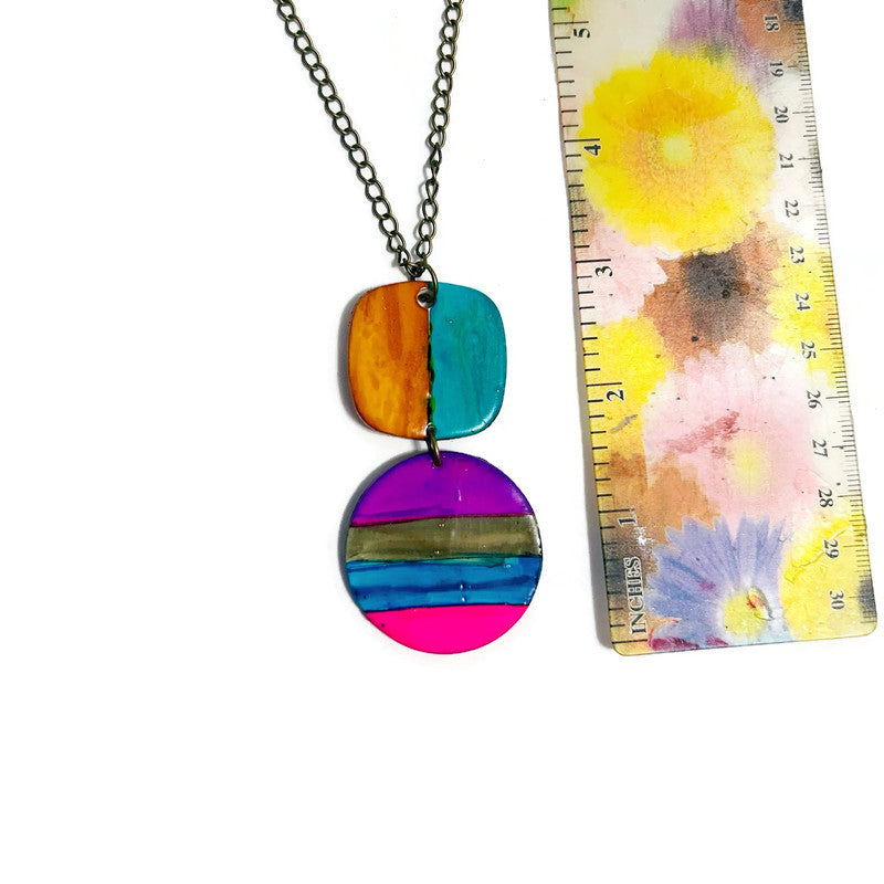 Colorful necklace with circular pendants next to a floral card and ruler for size reference