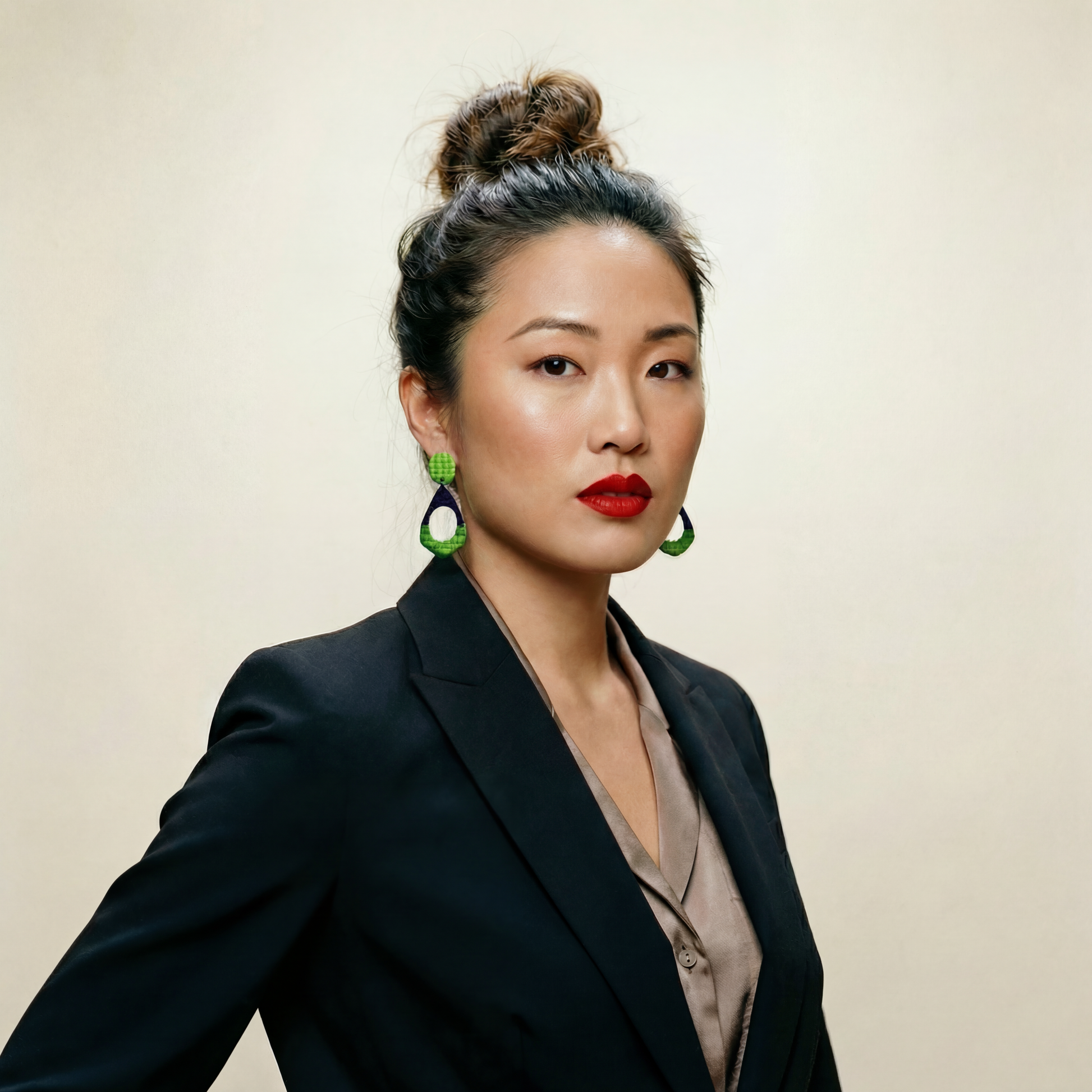 Woman wearing a black blazer and green and blue earrings against a beige background