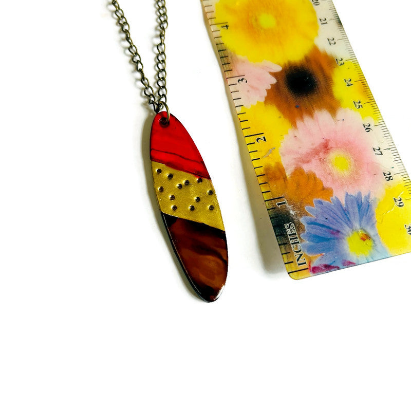 Colorful pendant necklace next to a floral-patterned ruler on a white background