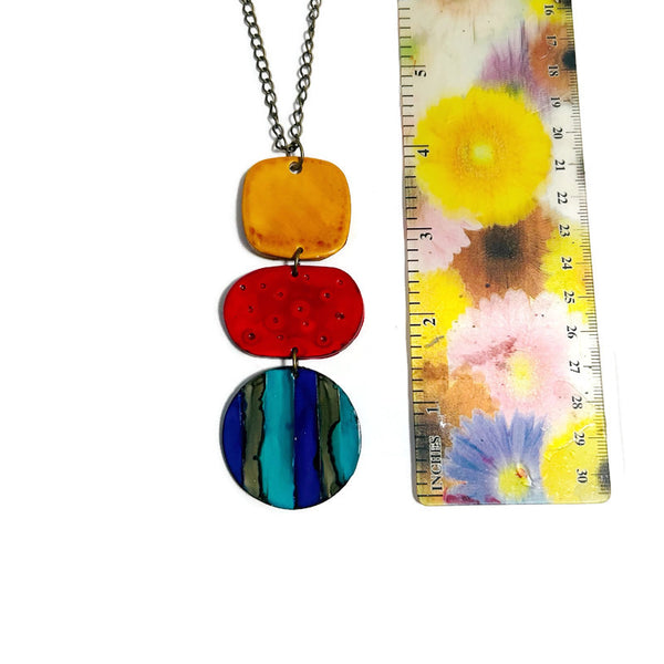 Colorful pendant necklace next to a floral-patterned ruler on a white background
