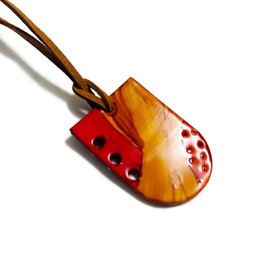 Clay pendant with red accents and holes on a white background