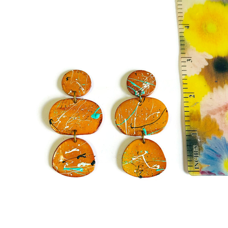 Pair of mustard yellow abstract earrings next to a ruler for size reference on a floral background.