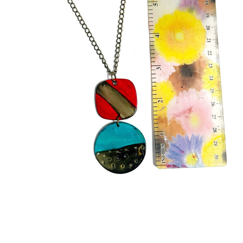Colorful necklace with round pendant next to a floral-patterned ruler on a white background