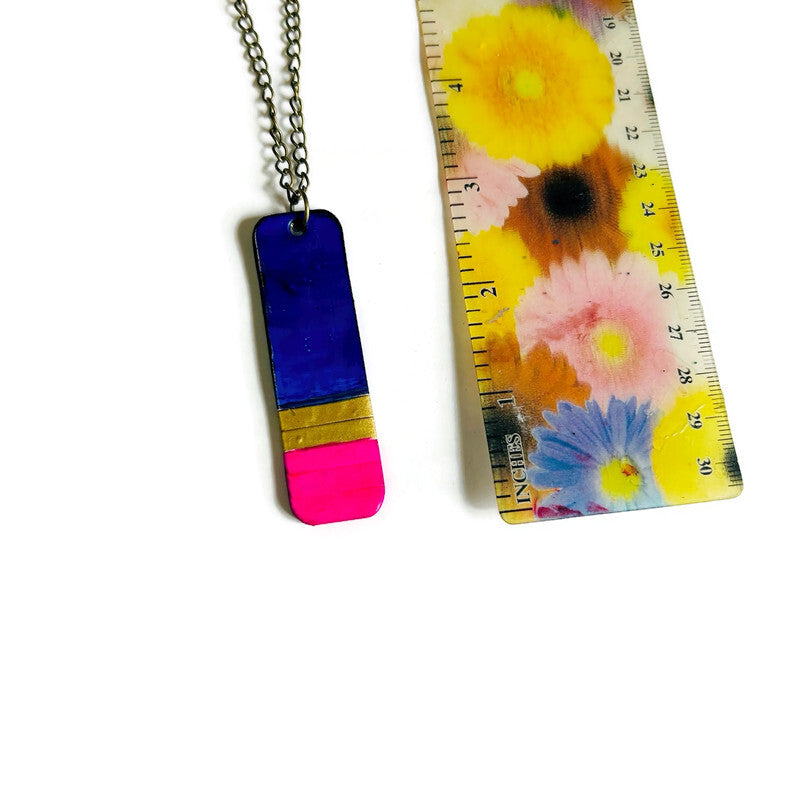 Colorful pendant necklace next to a floral-patterned ruler on a white background