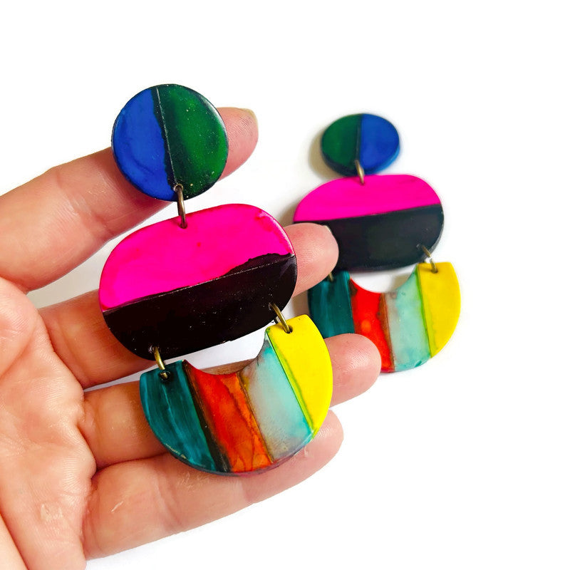 Colorful earrings held in a hand against a white background