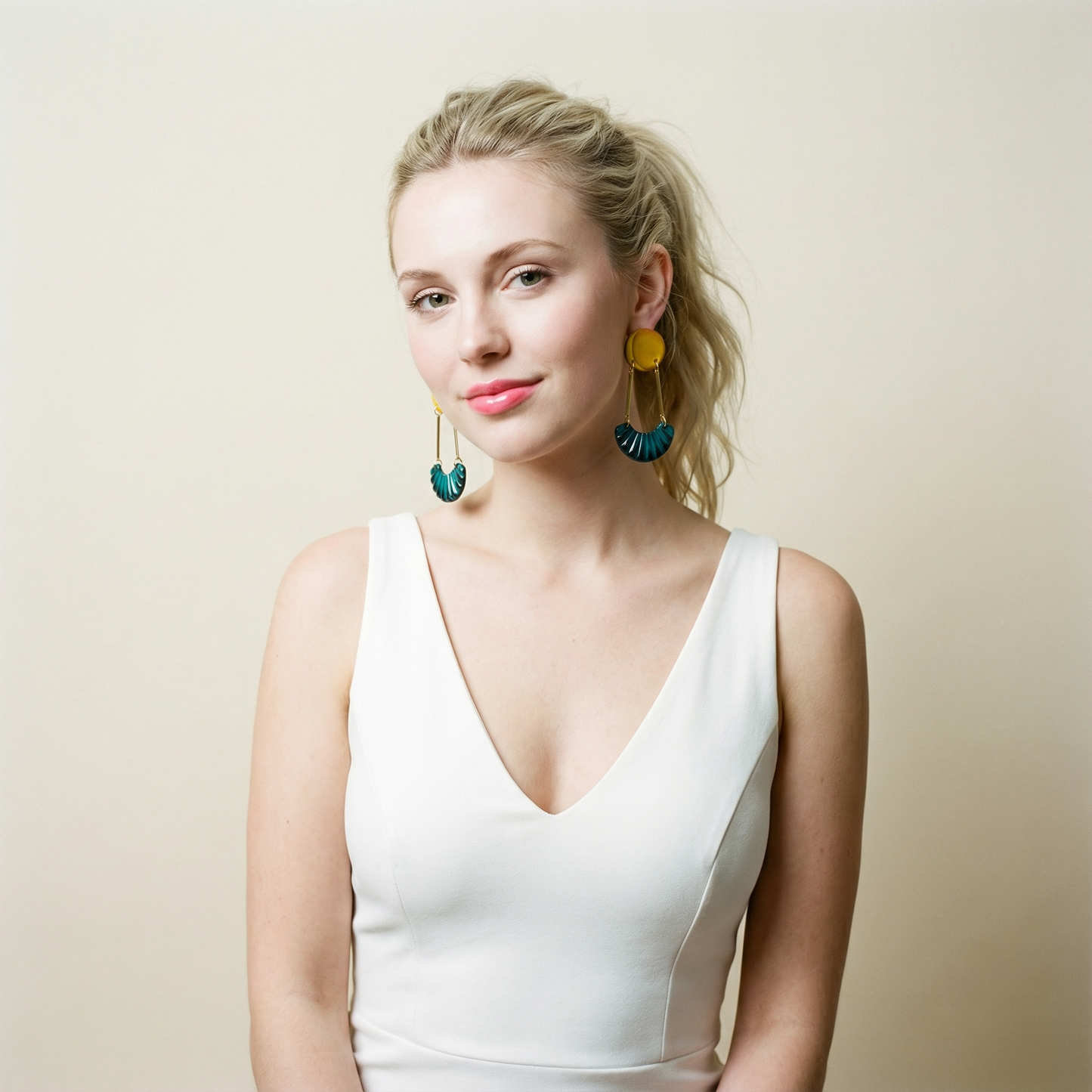 Woman wearing a white dress and colorful earrings against a beige background