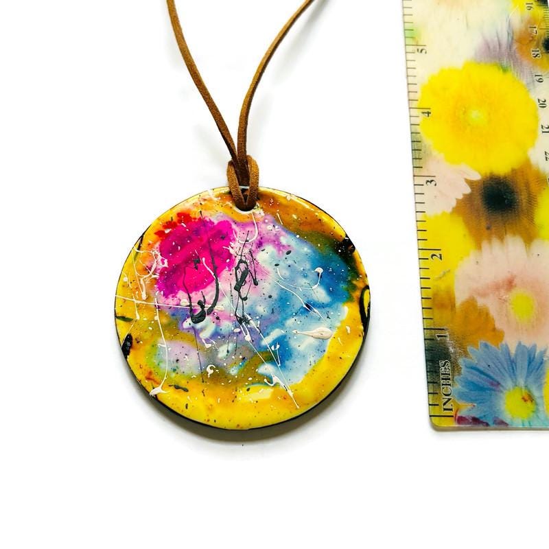 Colorful pendant with a floral design next to a ruler on a white background