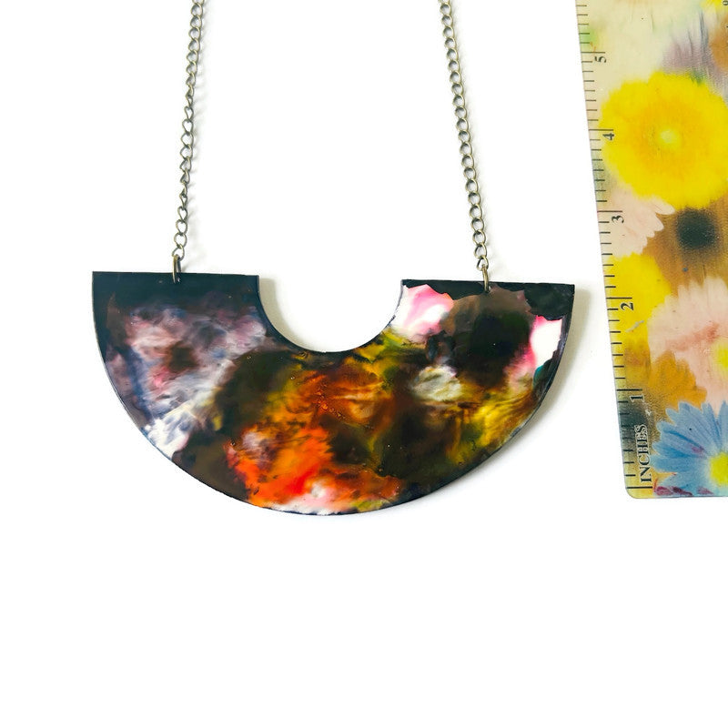 Colorful half-circle pendant necklace next to a floral-patterned ruler on a white background