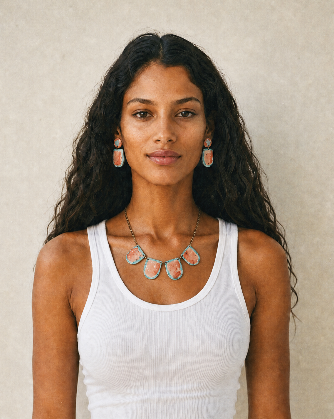 Woman wearing a white tank top and colorful necklace against a beige background