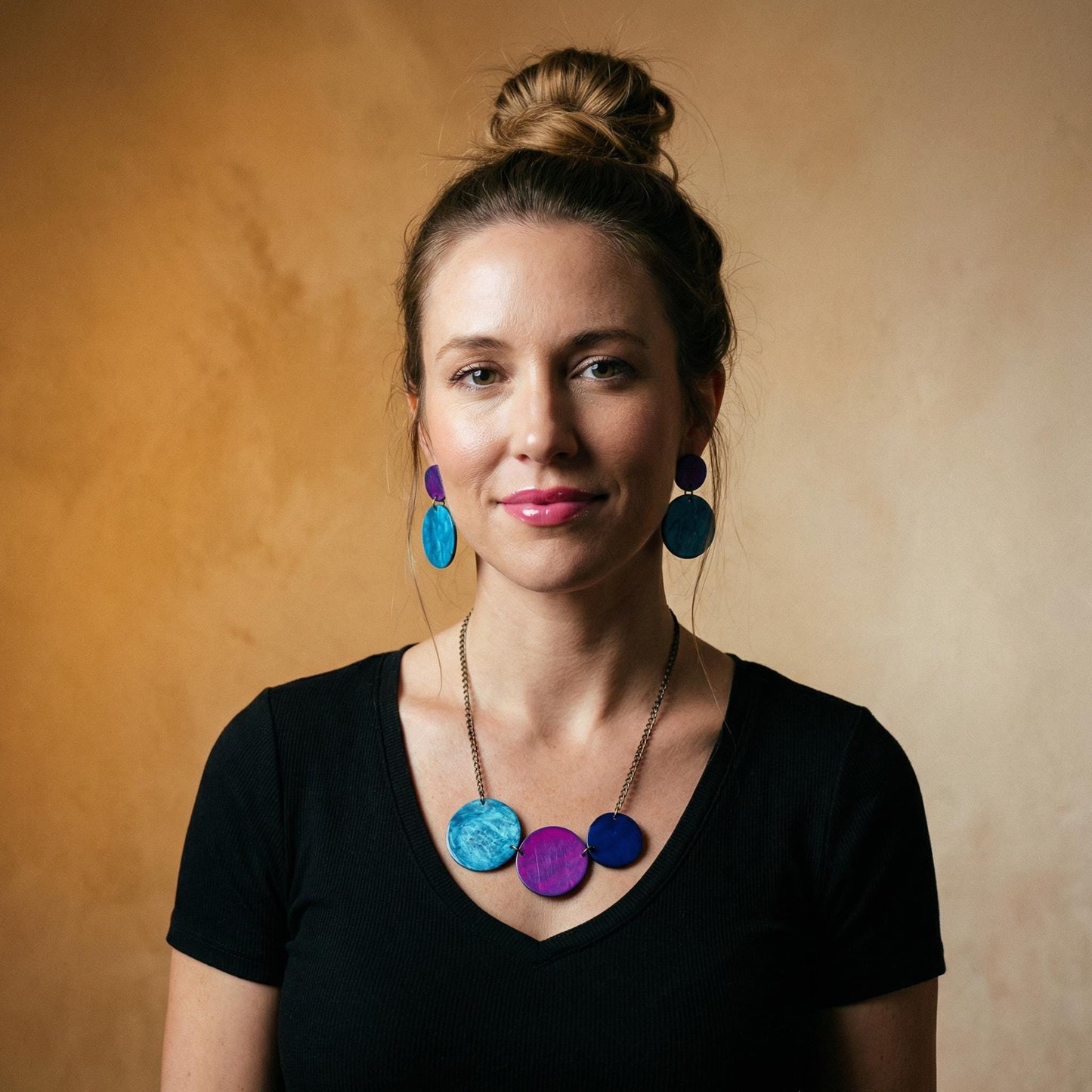 Woman wearing colorful earrings and a necklace against a beige background
