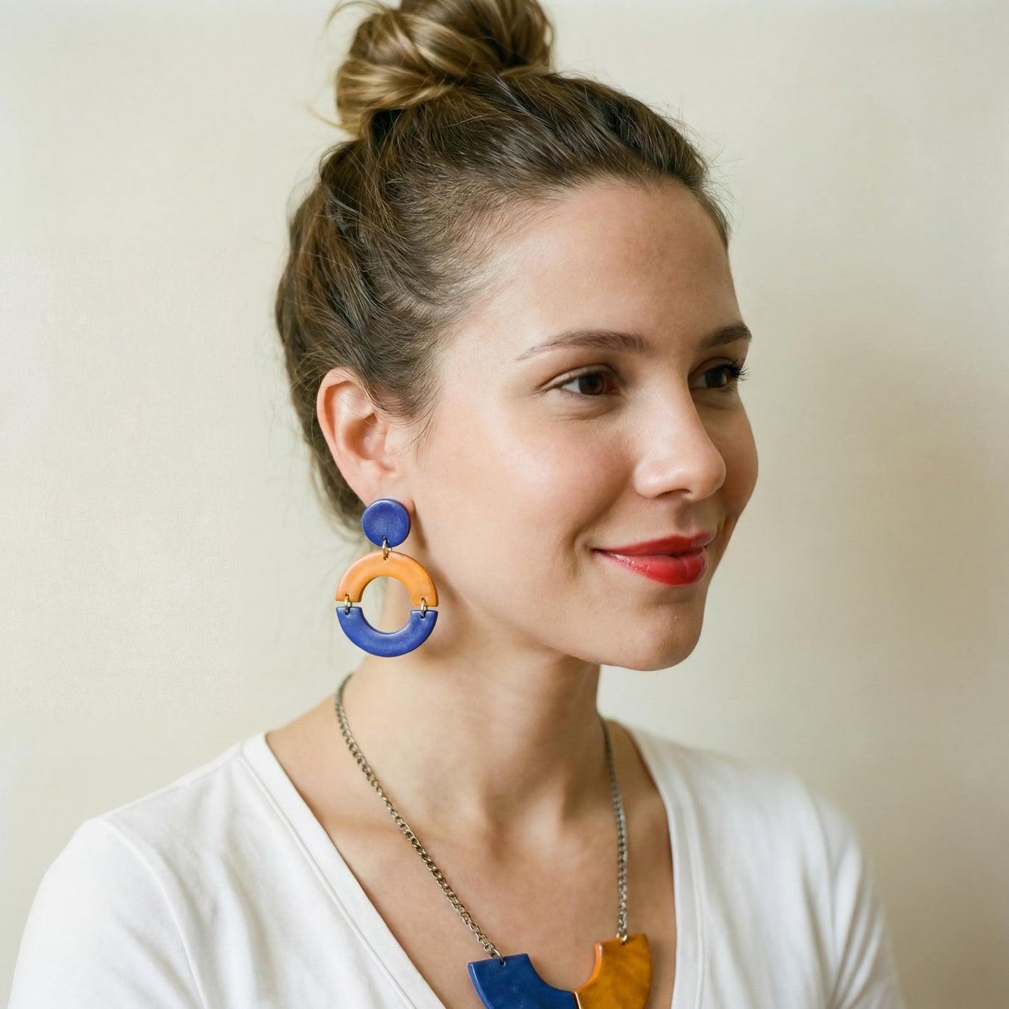 Woman wearing colorful earrings and a necklace against a plain background