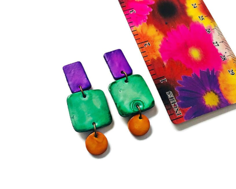 Colorful earrings with square and round components against a ruler