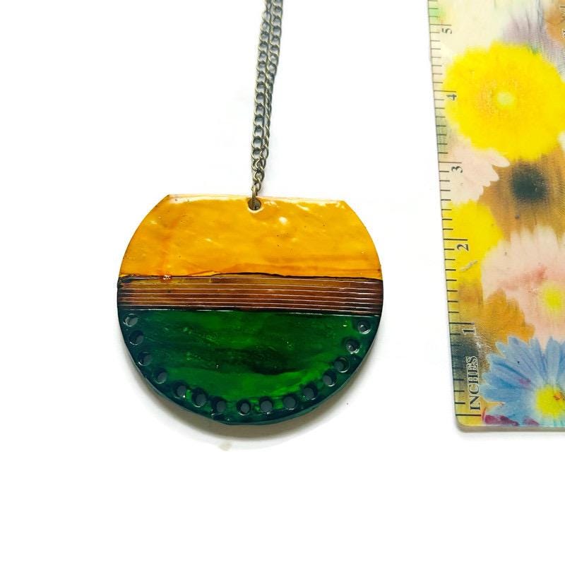 Round pendant with yellow and green design on a chain, next to a floral-patterned ruler.