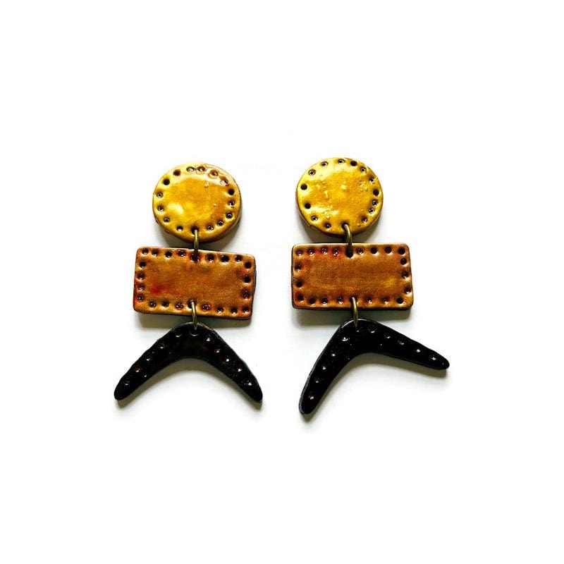 Pair of geometric drop earrings: round yellow stud, copper rectangle, black tail dangles.