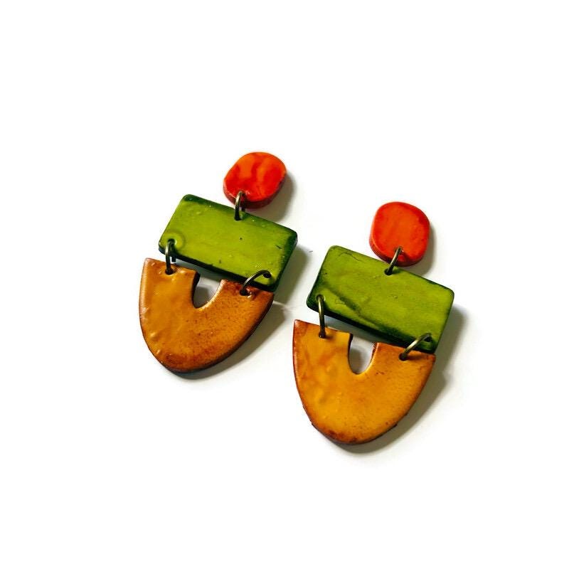Pair of colorful earrings with green, orange, and yellow elements on a white background