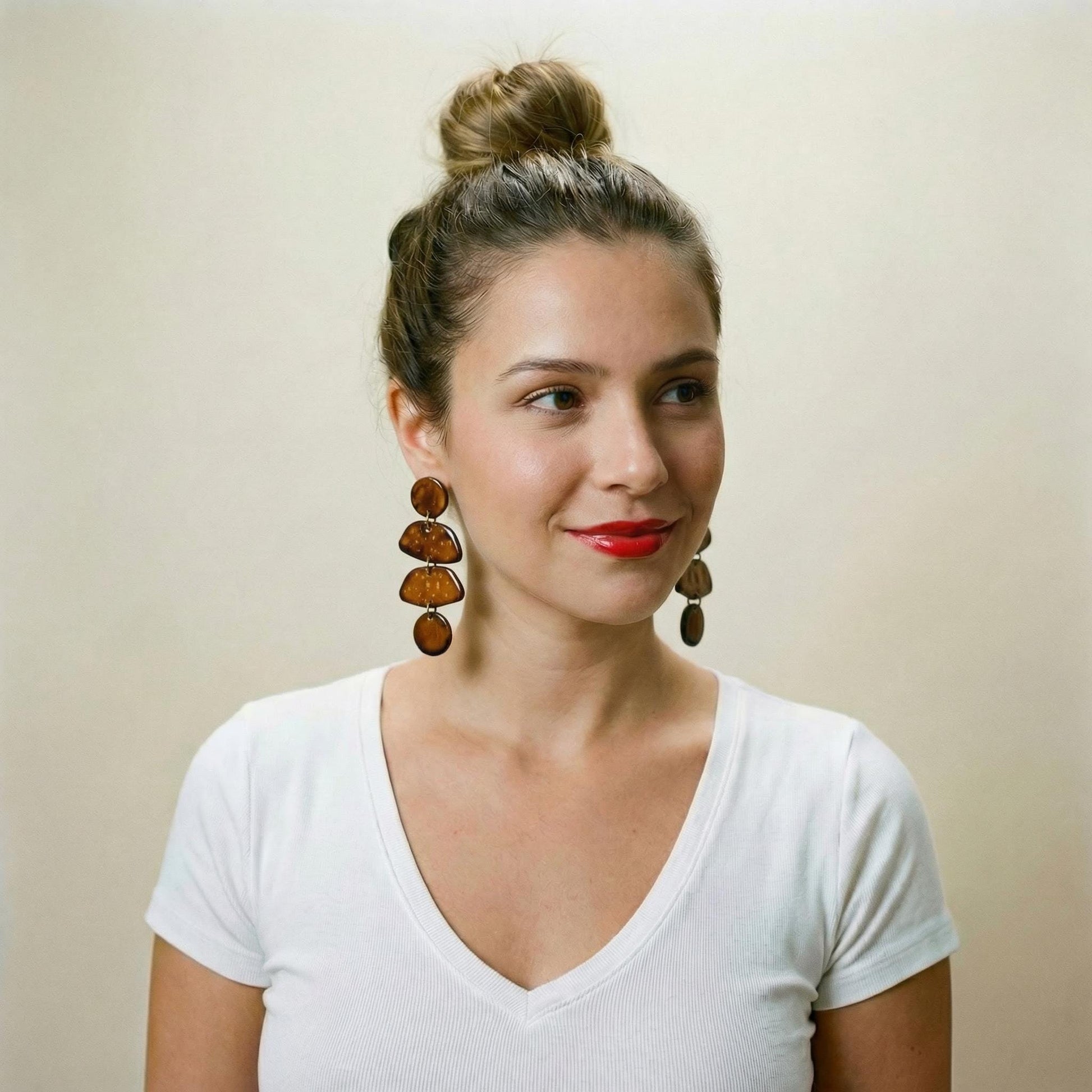 Woman wearing a white shirt and large earrings against a beige background