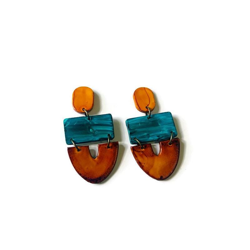 Pair of earrings with yellow, teal and brown design on a white background
