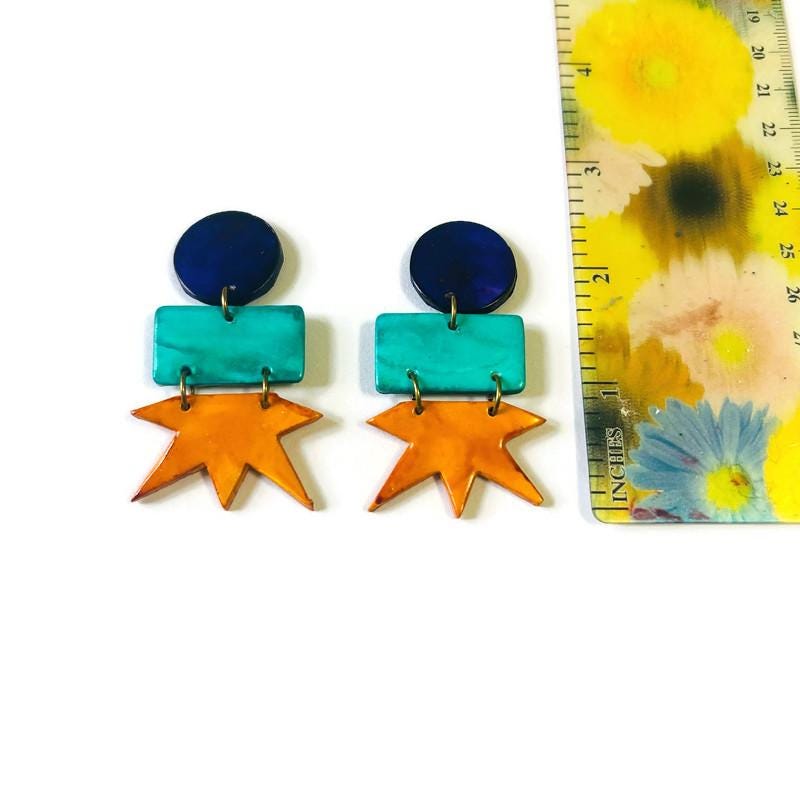 Geometric star drop earrings with dark blue round tops, teal blocks, and orange stars