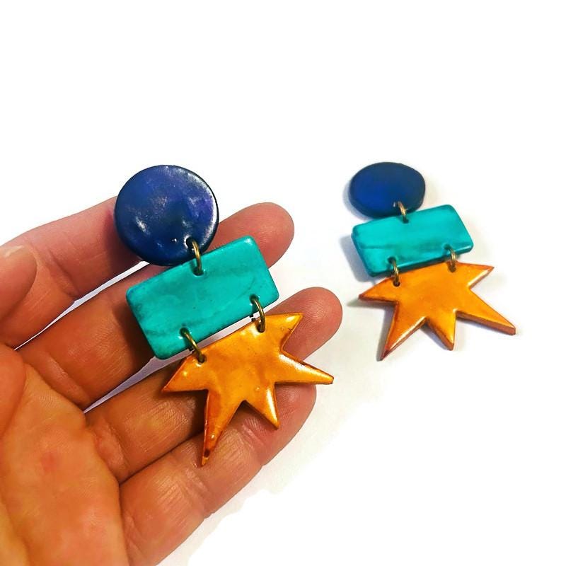 Geometric star drop earrings shown in hand: dark blue, teal, and orange star shapes