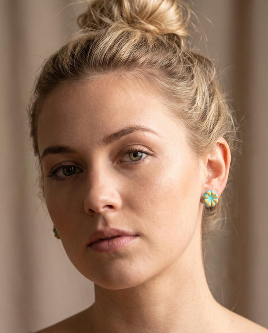 Teal and yellow floral stud earrings on model, small flower studs