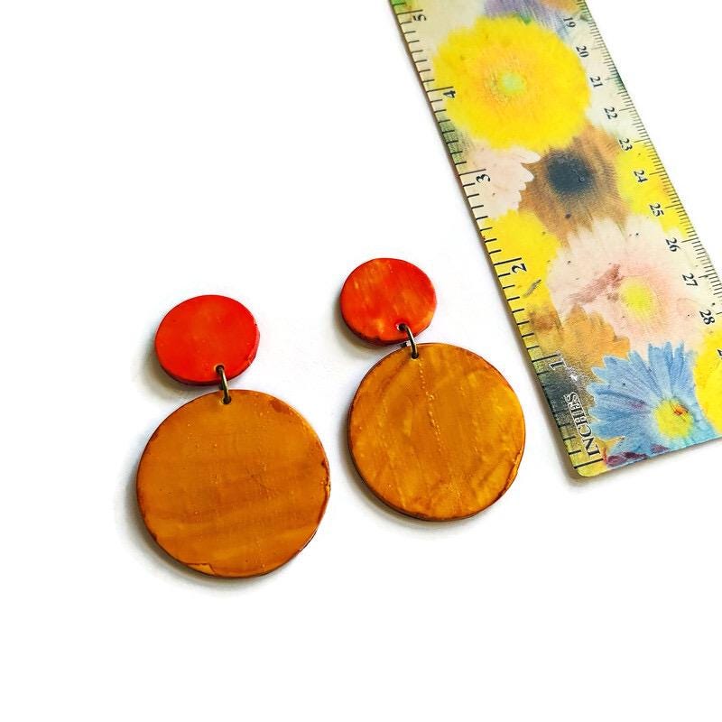 Pair of yellow earrings with a floral-patterned ruler for scale on a white background