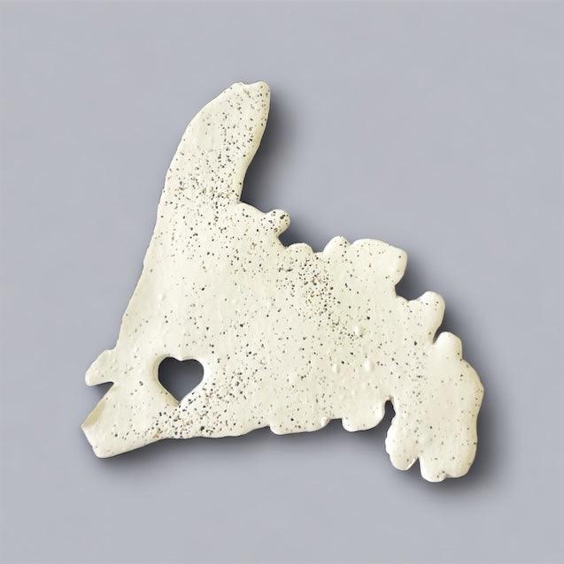 Speckled off-white PEI-shaped fridge magnet with heart cutout, angled front view.