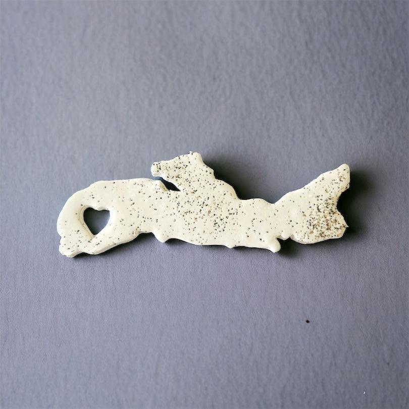 Off-white speckled PEI-shaped fridge magnet with heart cutout.