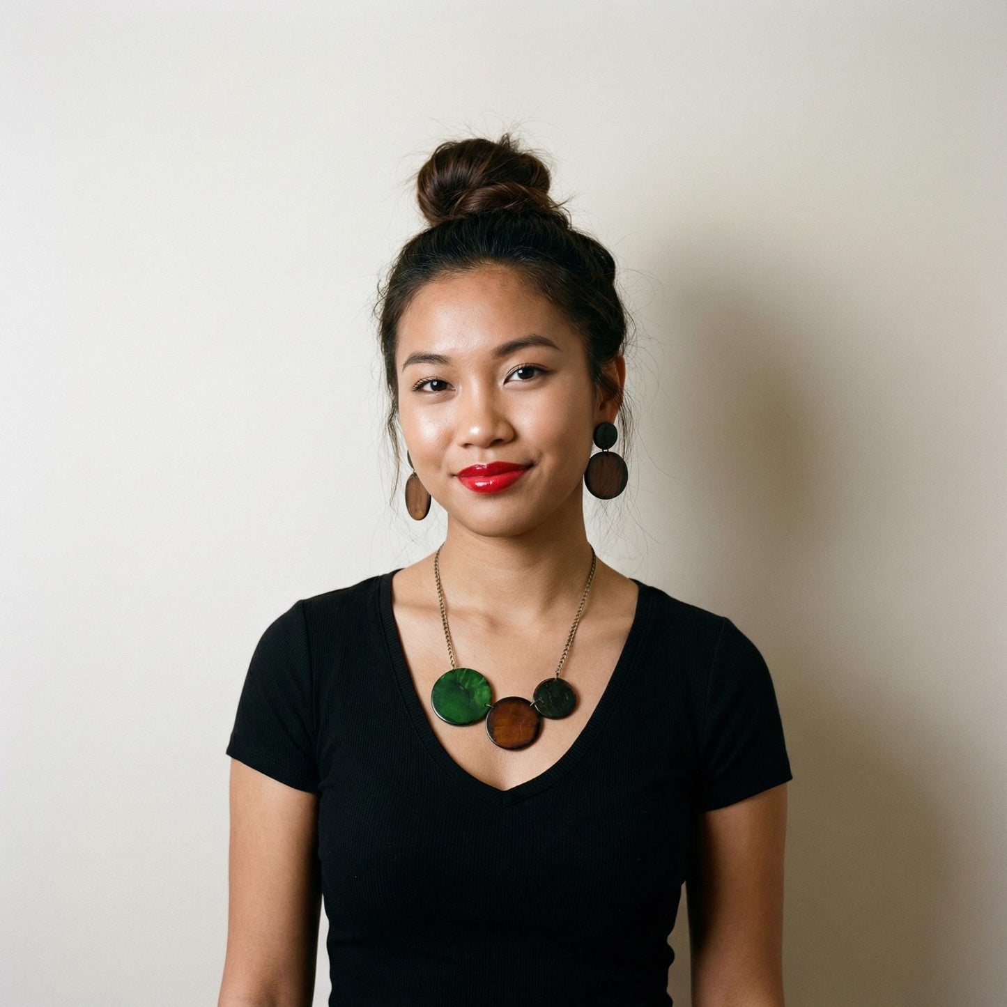 Woman wearing a black top with a necklace and earrings against a plain background