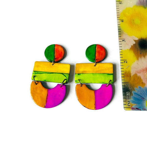 Colorful earrings with a ruler for scale on a white background