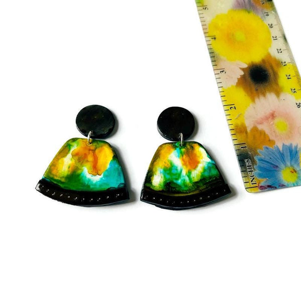 Colorful tie-dye earrings with black accents on a white background, next to a floral-patterned ruler.