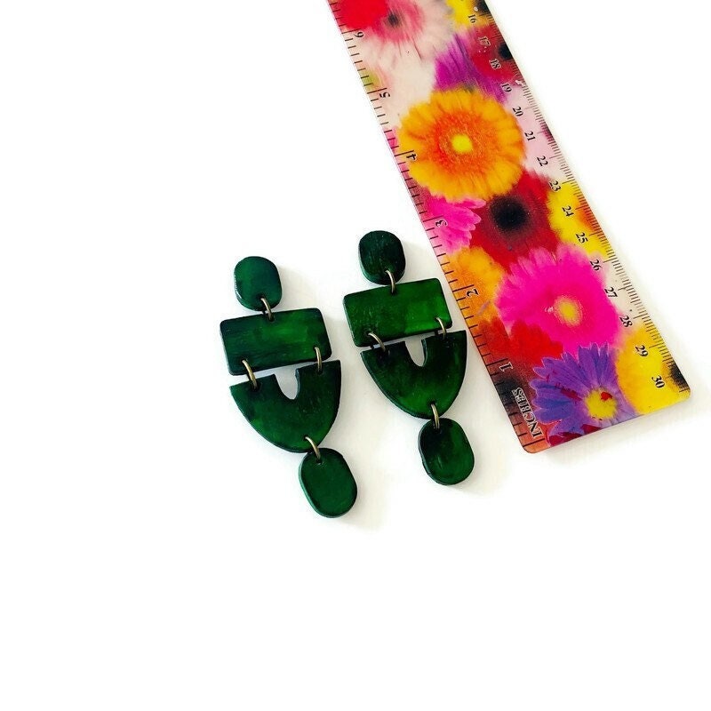 forest green statement earrings against ruler